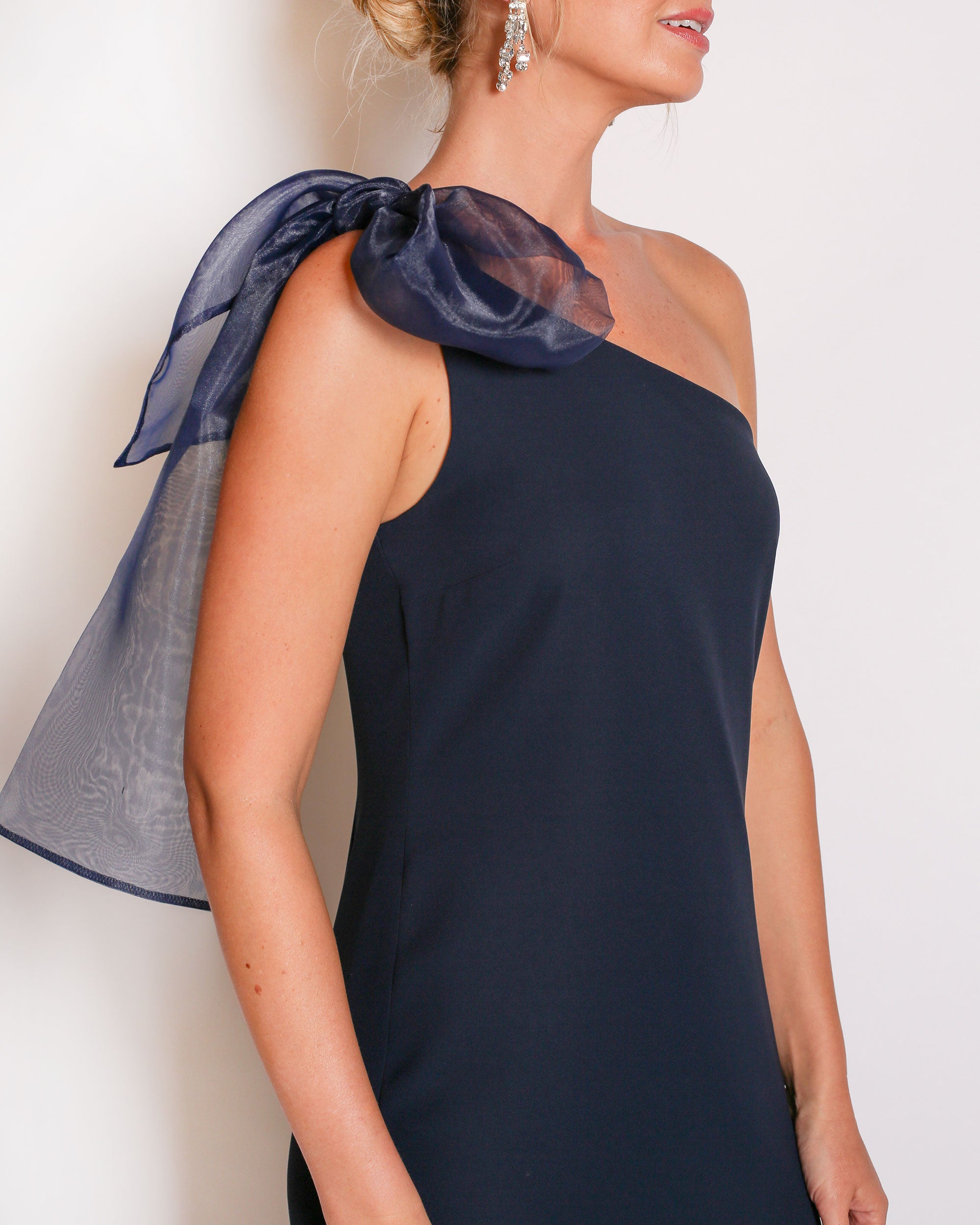Navy one-shoulder gown with a large bow detail on a white background